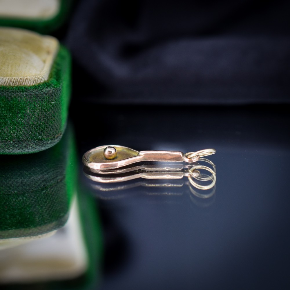 A small antique 9ct rose gold charm shaped like a tennis racket with a raised central tennis ball. View IV