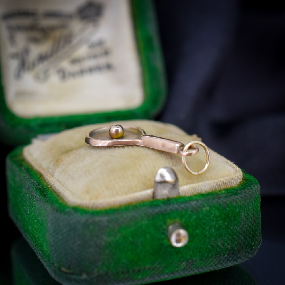 A small antique 9ct rose gold charm shaped like a tennis racket with a raised central tennis ball. View VII