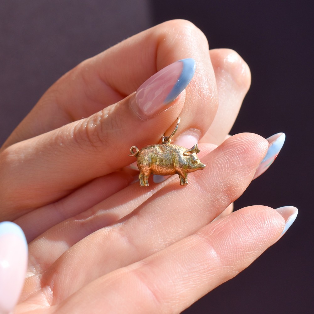 An Edwardian 9ct yellow gold pig charm featuring a textured three-dimensional body and an attached suspension ring. View V