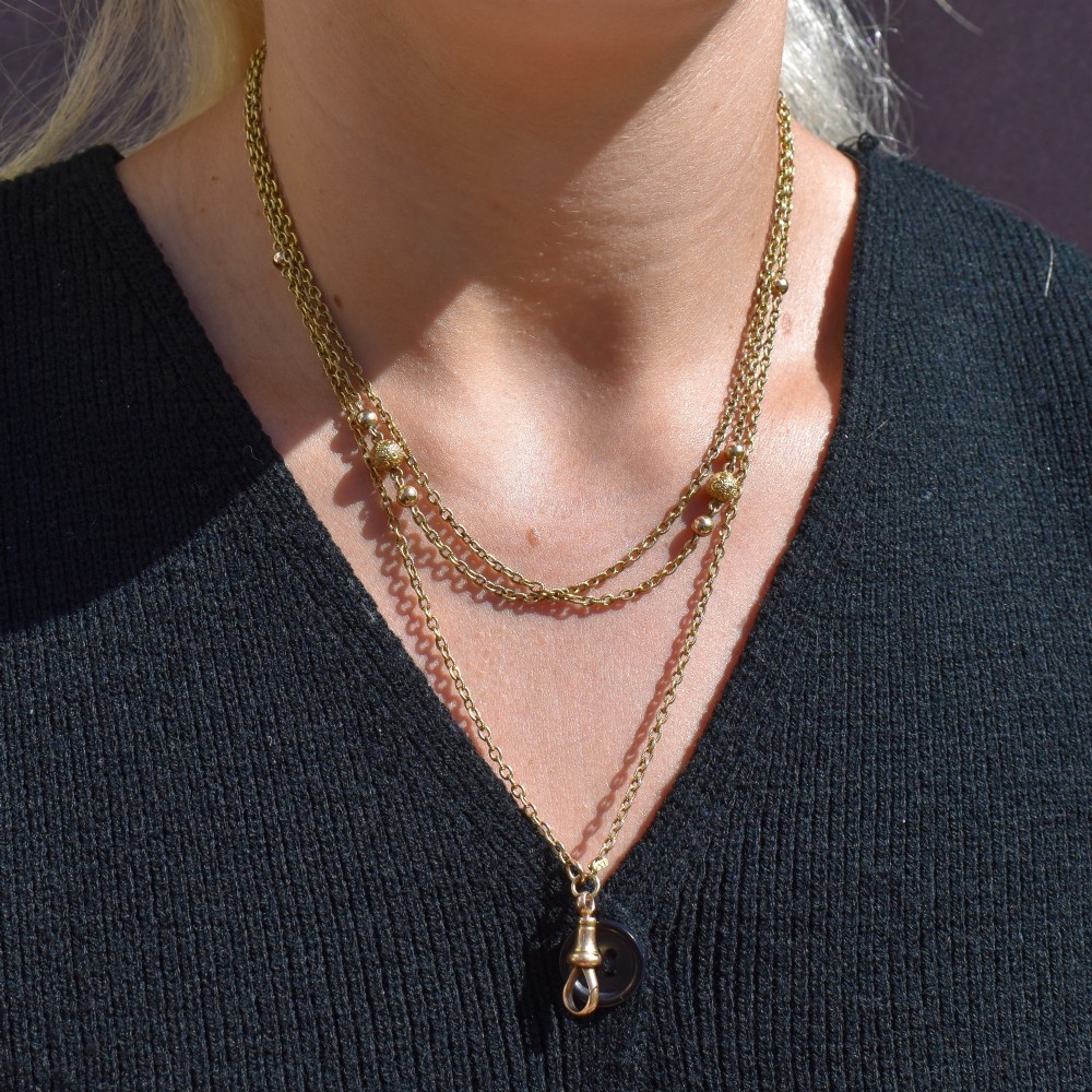 An antique 9ct yellow gold curb link guard chain layered in multiple loops with a dog clip fastener on a black bust. View X