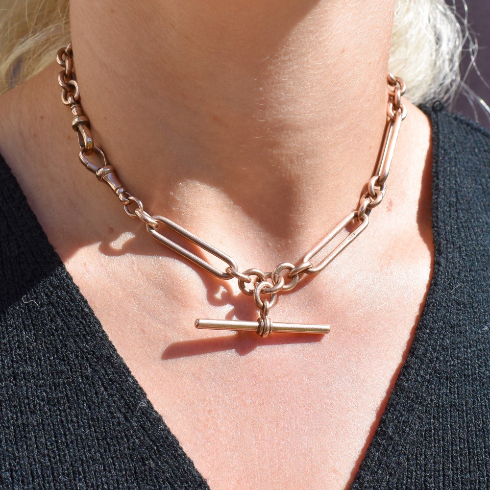 An Edwardian 9ct gold trombone link chain necklace with a central T-bar drop and dog clip clasp. View X