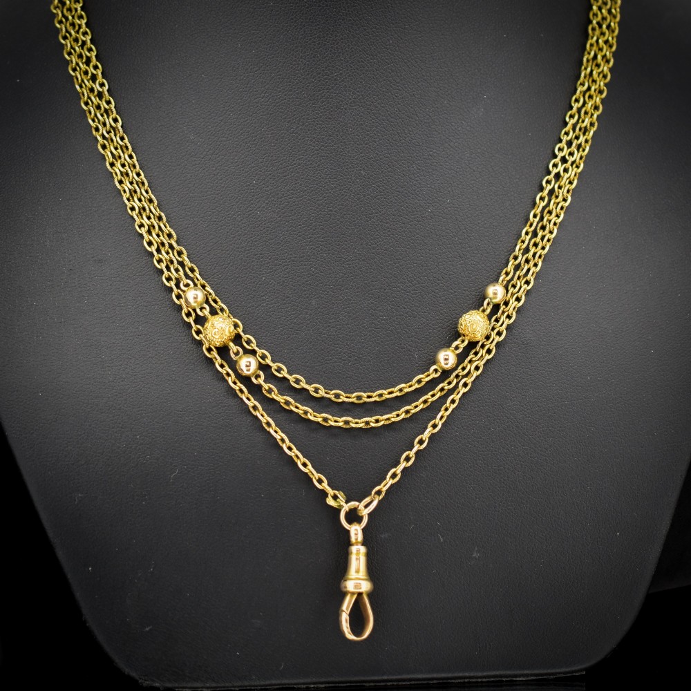 An antique Victorian 15ct yellow gold long fancy link guard chain necklace styled in multiple tiers, featuring pattern-carved gold beads and a swivel clasp hanging at the centre.
