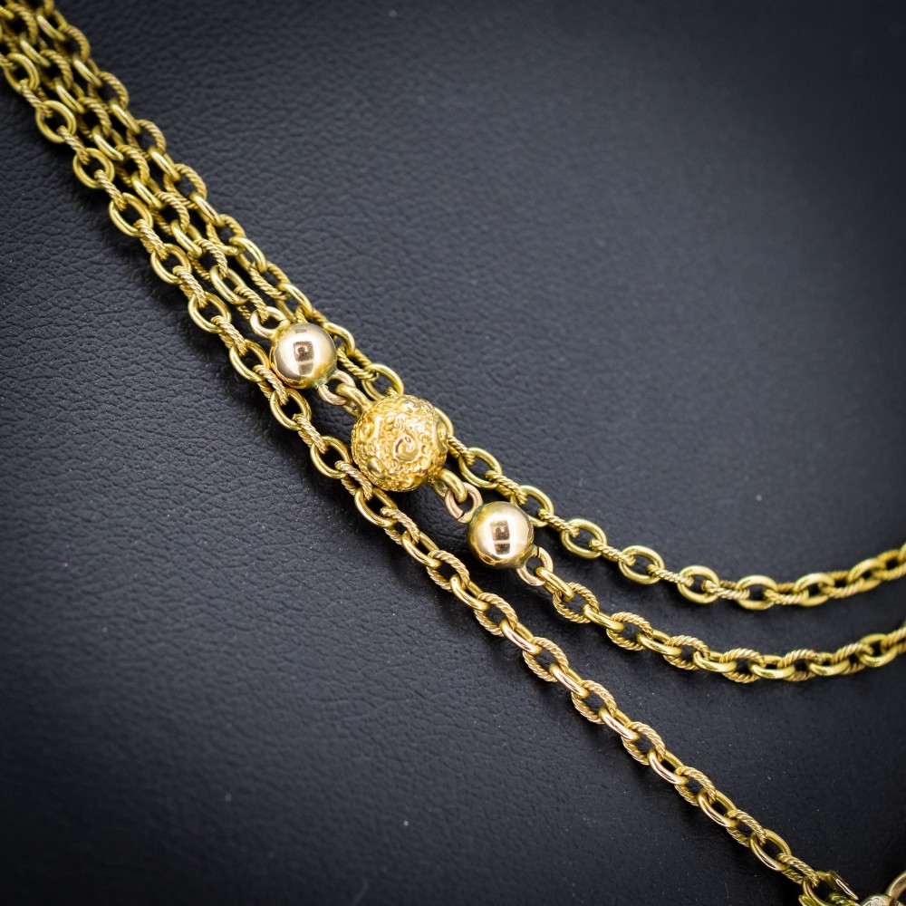 An antique Victorian 15ct yellow gold long fancy link guard chain necklace styled in multiple tiers, featuring pattern-carved gold beads and a swivel clasp hanging at the centre. View II