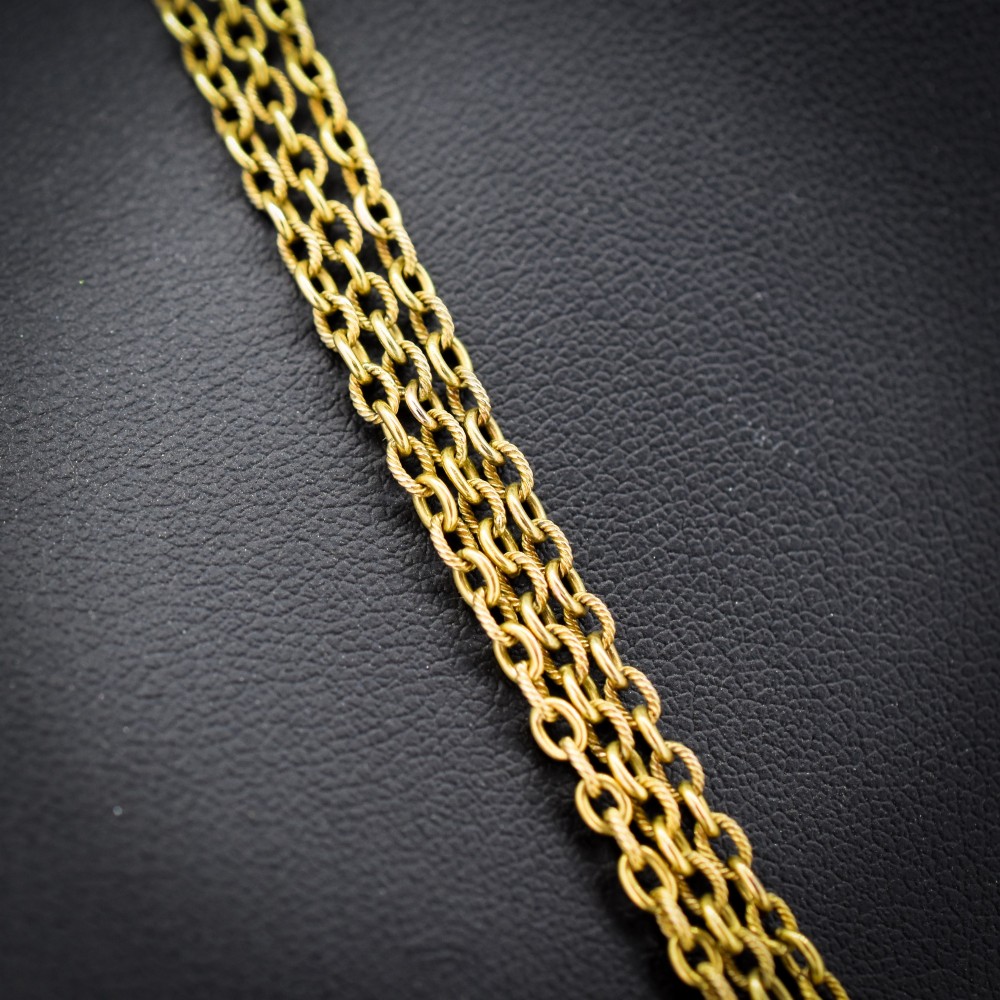 An antique Victorian 15ct yellow gold long fancy link guard chain necklace styled in multiple tiers, featuring pattern-carved gold beads and a swivel clasp hanging at the centre. View III