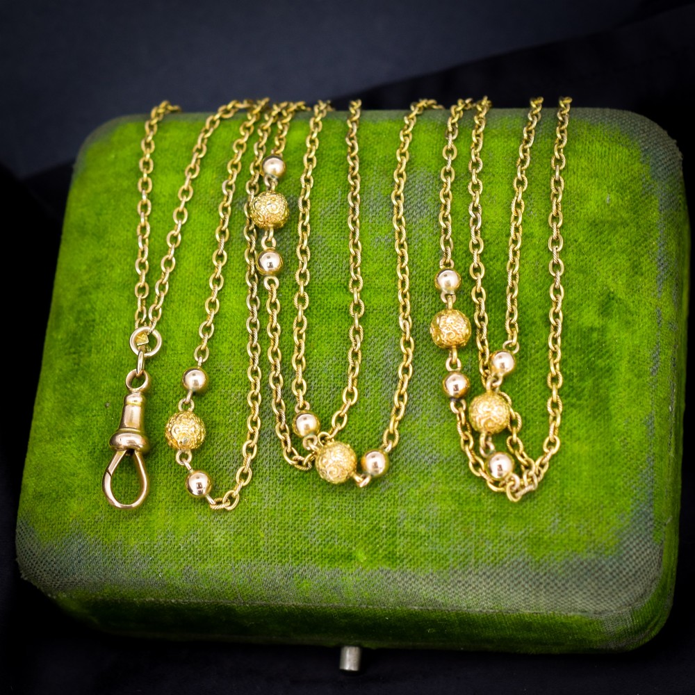 An antique Victorian 15ct yellow gold long fancy link guard chain necklace styled in multiple tiers, featuring pattern-carved gold beads and a swivel clasp hanging at the centre. View IV
