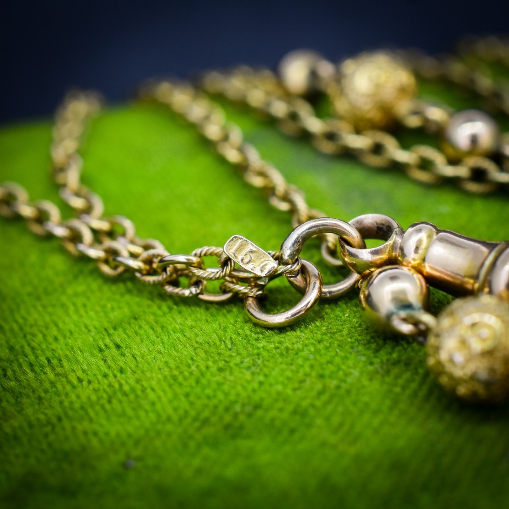 An antique Victorian 15ct yellow gold long fancy link guard chain necklace styled in multiple tiers, featuring pattern-carved gold beads and a swivel clasp hanging at the centre. View VI