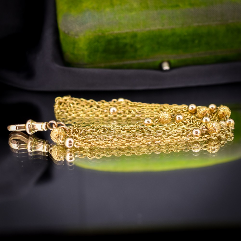 An antique Victorian 15ct yellow gold long fancy link guard chain necklace styled in multiple tiers, featuring pattern-carved gold beads and a swivel clasp hanging at the centre. View VII