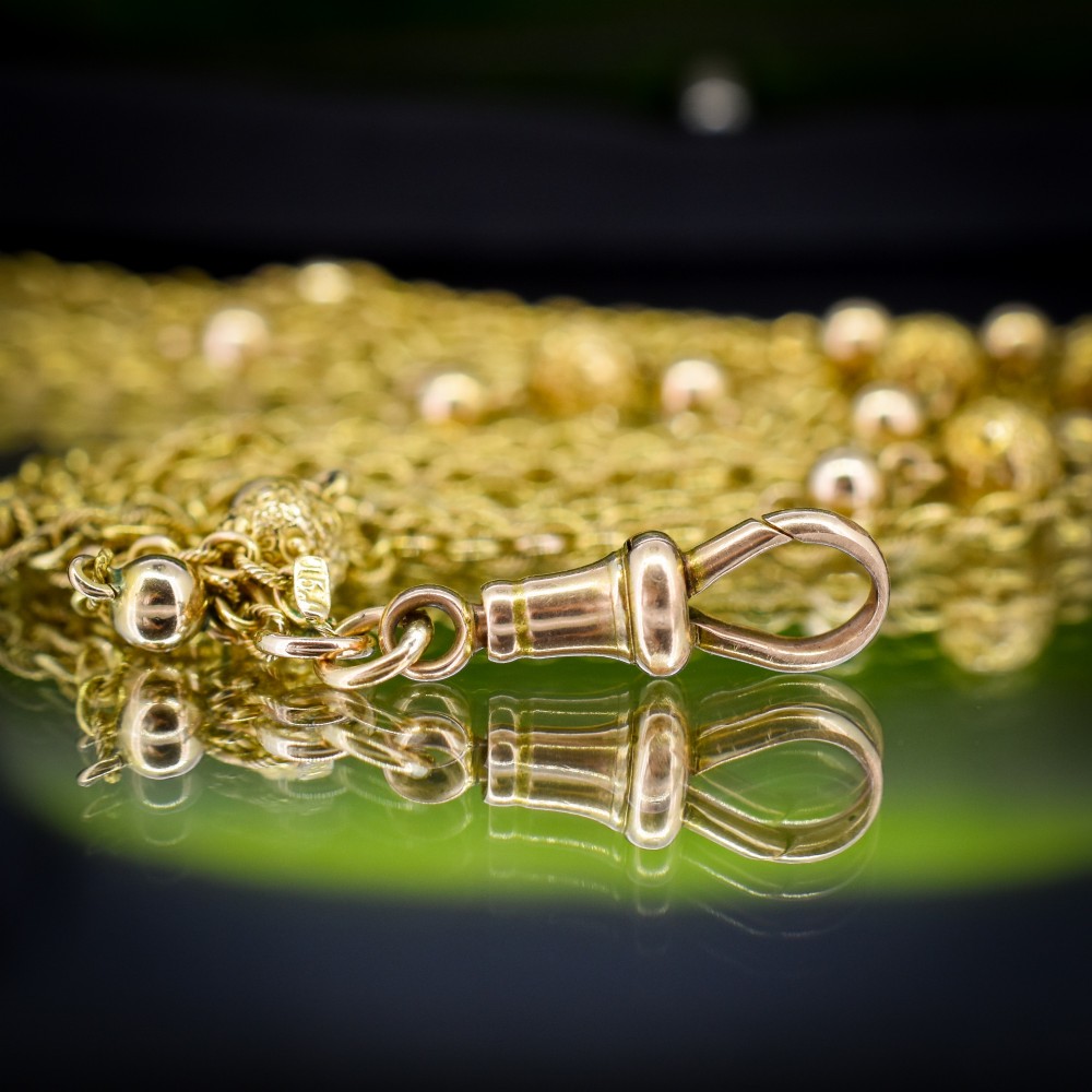 An antique Victorian 15ct yellow gold long fancy link guard chain necklace styled in multiple tiers, featuring pattern-carved gold beads and a swivel clasp hanging at the centre. View VIII