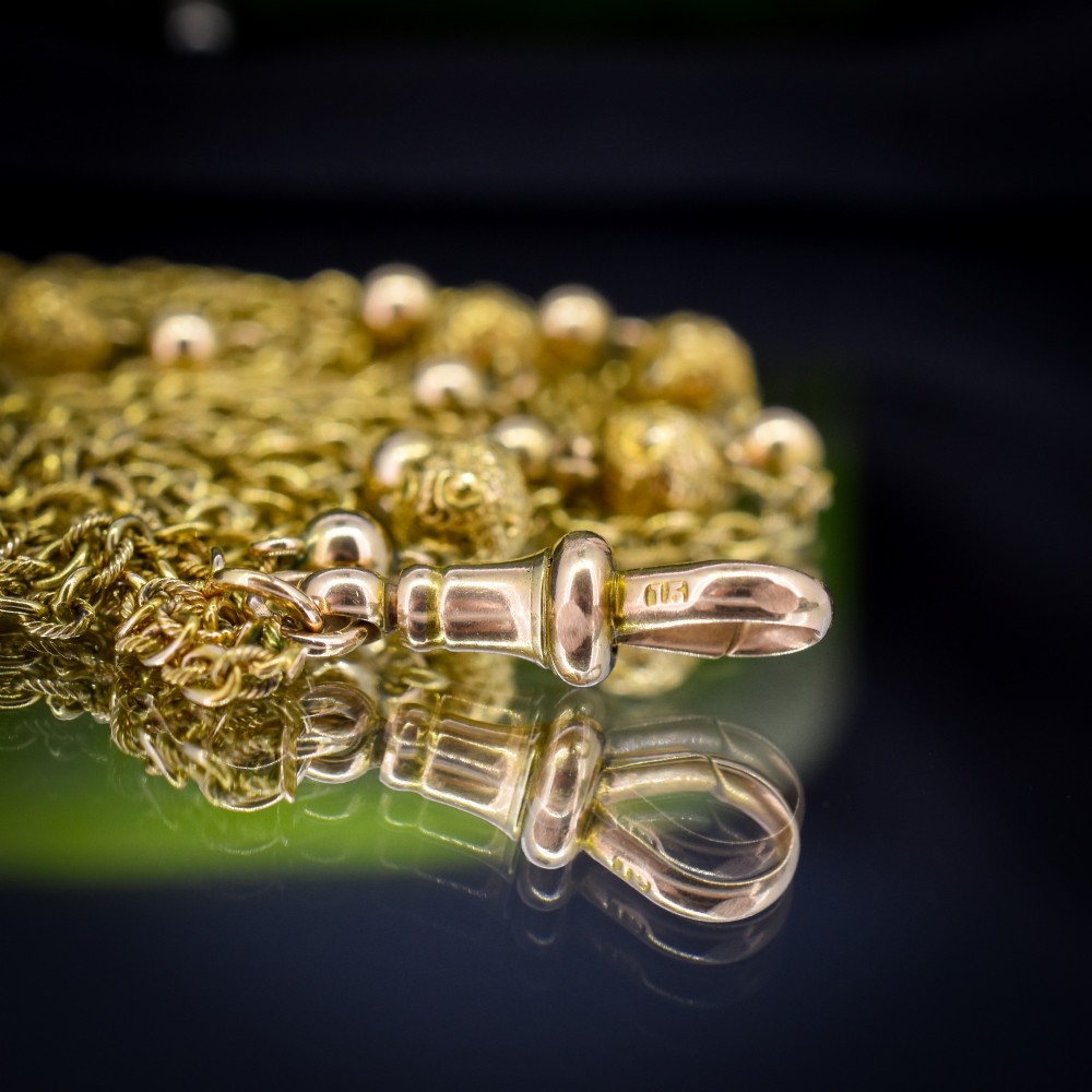 An antique Victorian 15ct yellow gold long fancy link guard chain necklace styled in multiple tiers, featuring pattern-carved gold beads and a swivel clasp hanging at the centre. View IX