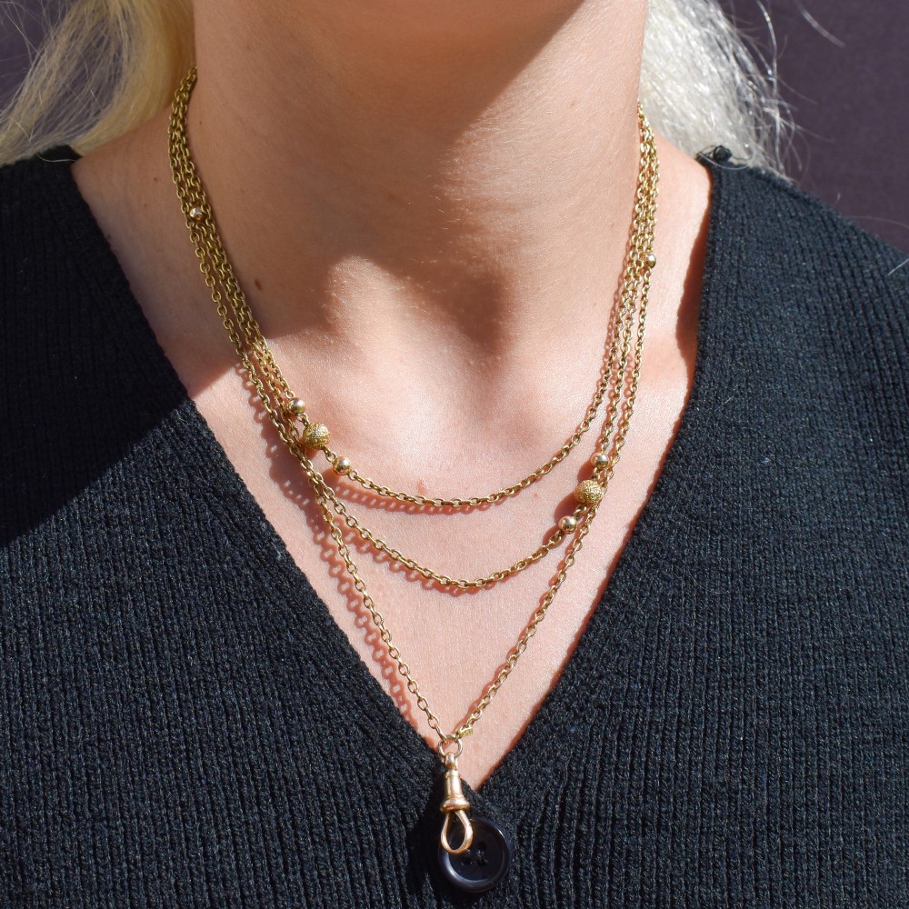 An antique Victorian 15ct yellow gold long fancy link guard chain necklace styled in multiple tiers, featuring pattern-carved gold beads and a swivel clasp hanging at the centre. View X