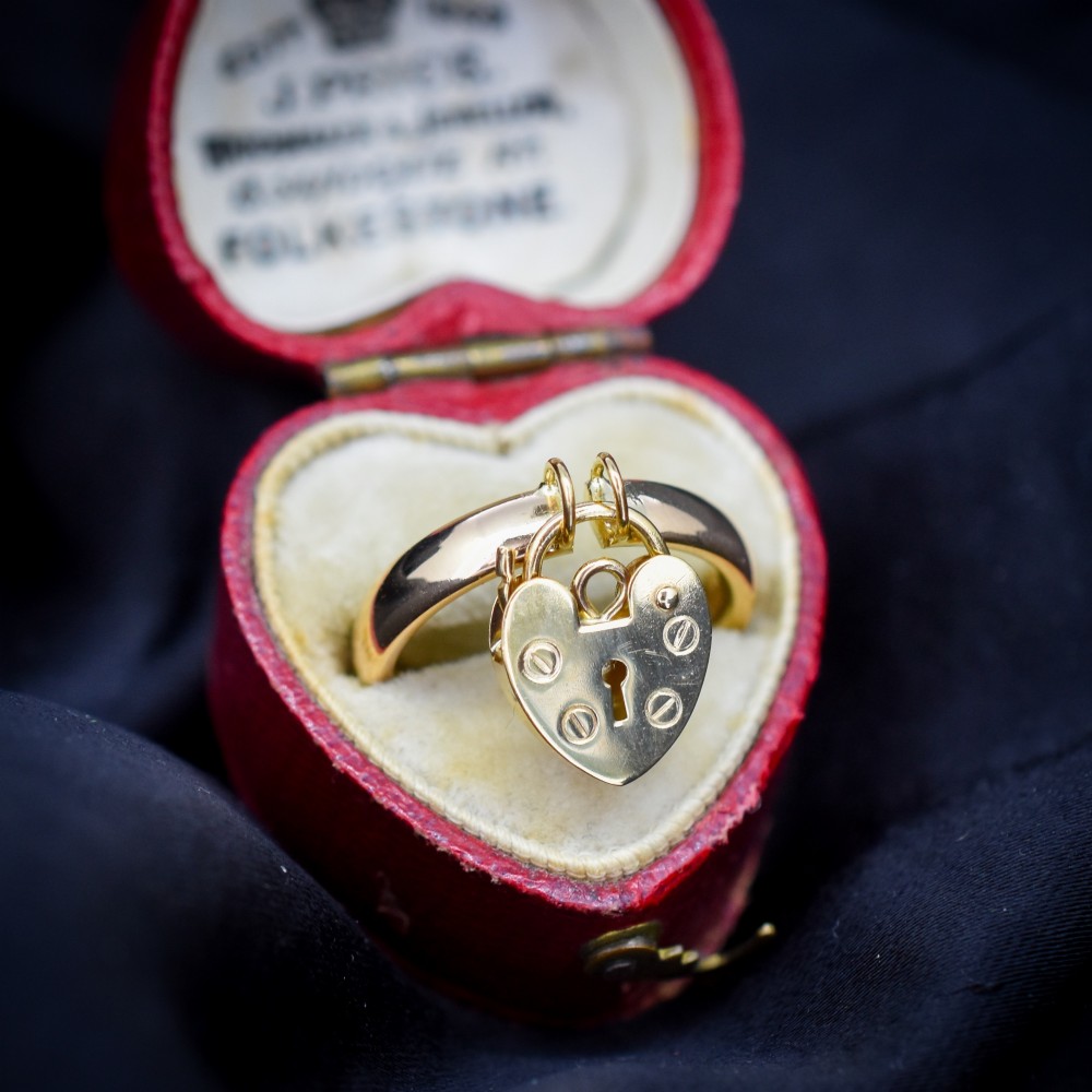 A polished 9ct yellow gold band ring featuring a suspended heart-shaped padlock drop charm with keyhole detail. View III