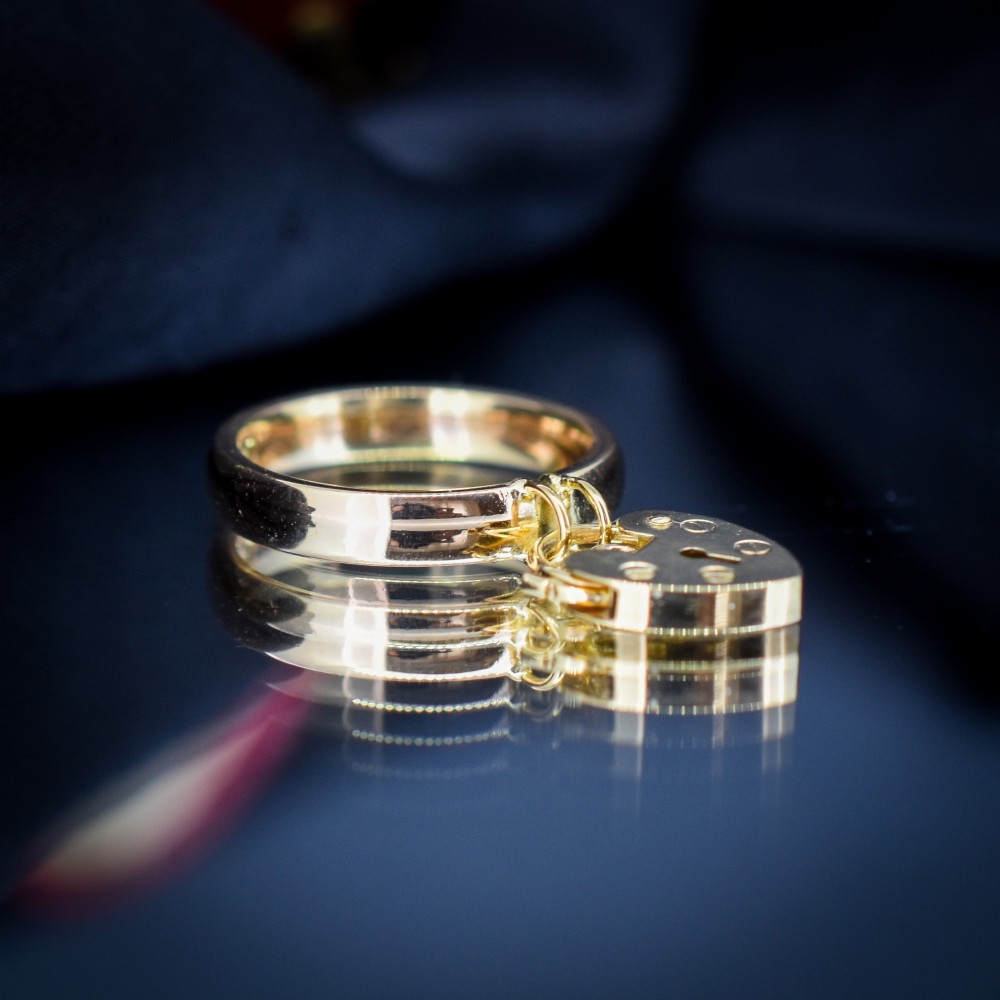A polished 9ct yellow gold band ring featuring a suspended heart-shaped padlock drop charm with keyhole detail. View IV