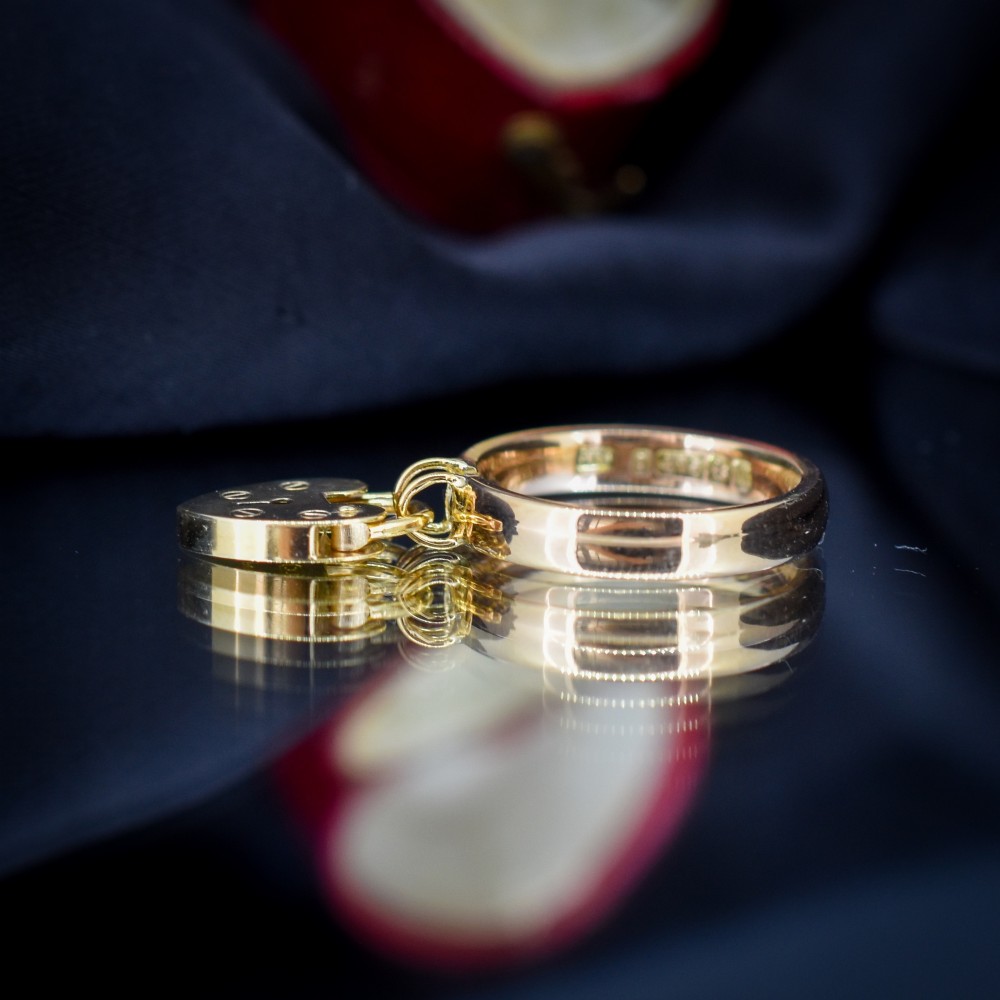 A polished 9ct yellow gold band ring featuring a suspended heart-shaped padlock drop charm with keyhole detail. View V