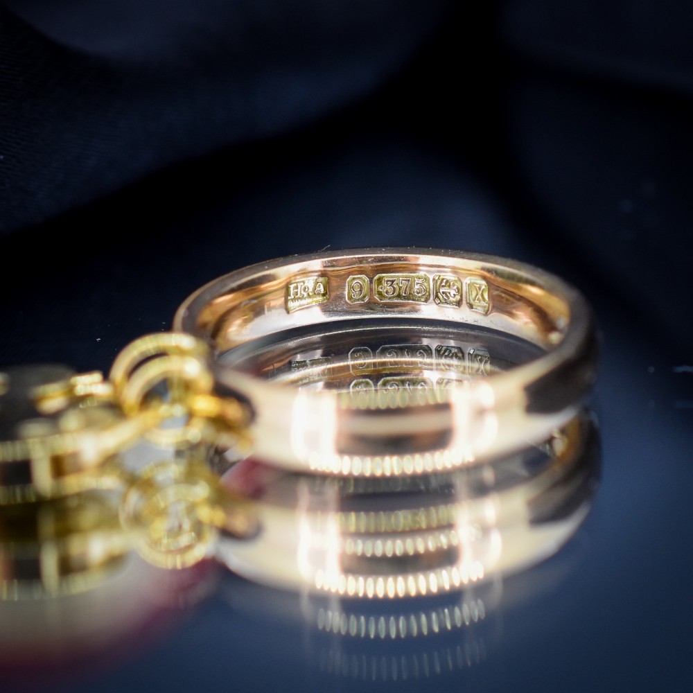 A polished 9ct yellow gold band ring featuring a suspended heart-shaped padlock drop charm with keyhole detail. View VI