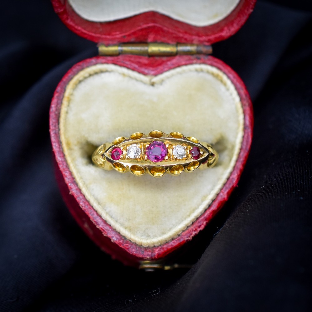 An antique 18ct yellow gold boat ring set with three round rubies alternating with two diamonds across a carved gallery setting.