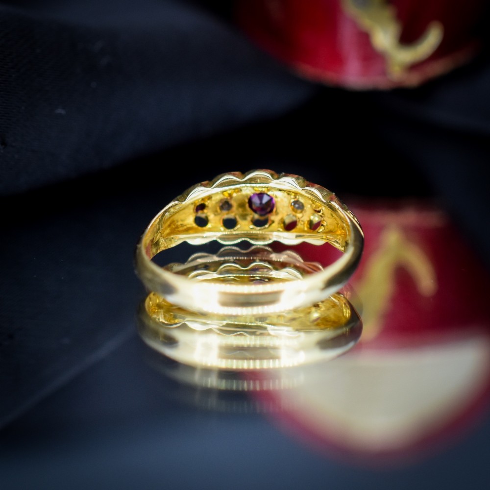 An antique 18ct yellow gold boat ring set with three round rubies alternating with two diamonds across a carved gallery setting. View IV