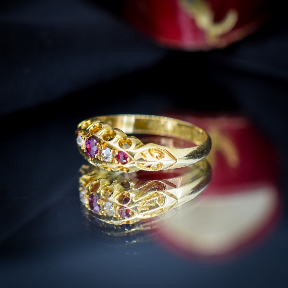 An antique 18ct yellow gold boat ring set with three round rubies alternating with two diamonds across a carved gallery setting. View V