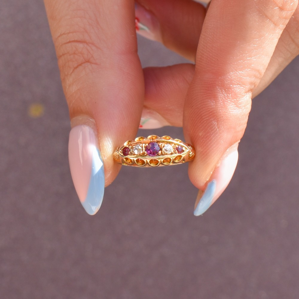 An antique 18ct yellow gold boat ring set with three round rubies alternating with two diamonds across a carved gallery setting. View VII