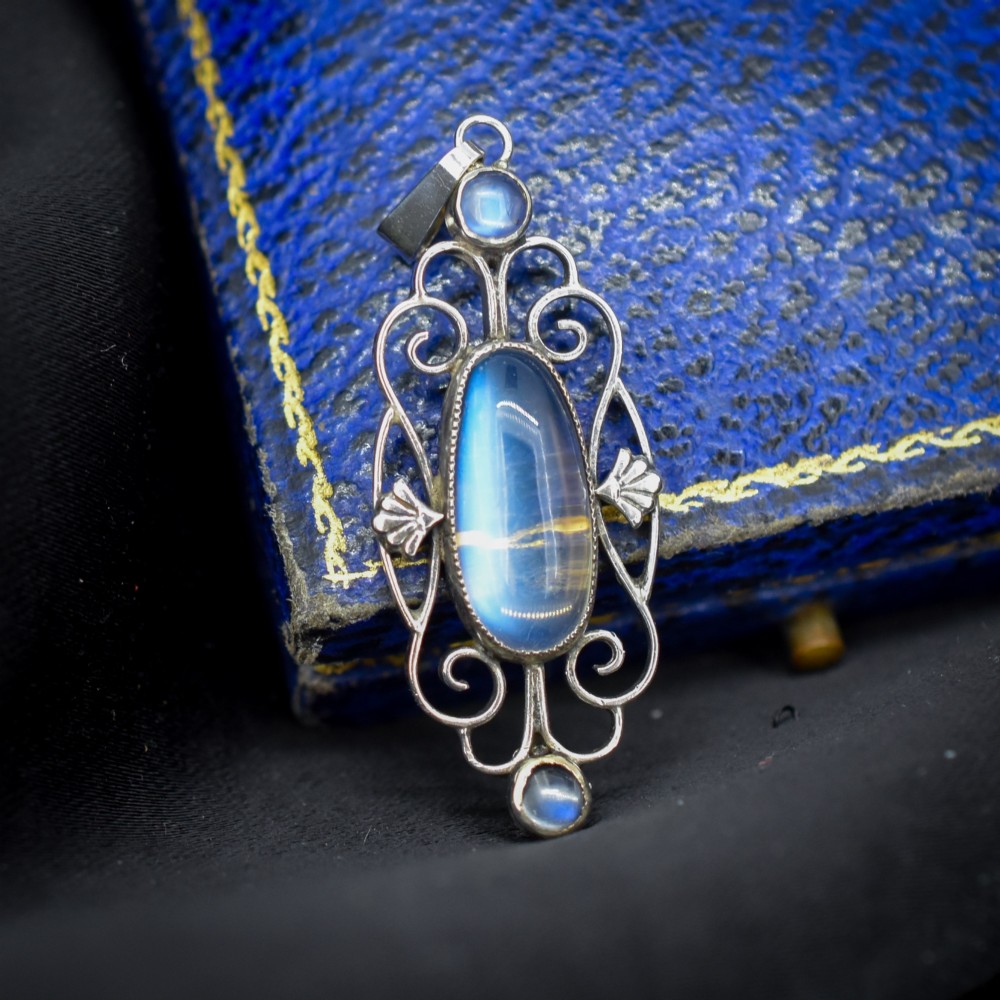 An antique sterling silver drop pendant featuring openwork scroll design set with an oval central moonstone cabochon and two smaller round moonstones. View III