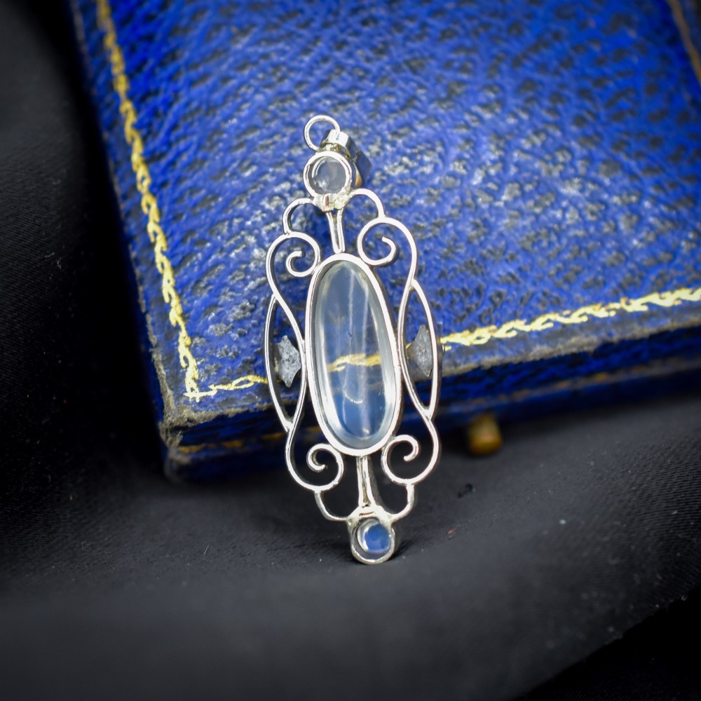 An antique sterling silver drop pendant featuring openwork scroll design set with an oval central moonstone cabochon and two smaller round moonstones. View IV