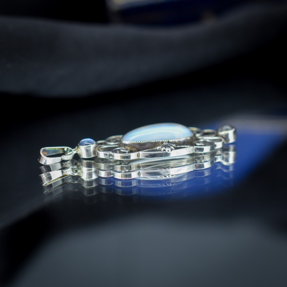 An antique sterling silver drop pendant featuring openwork scroll design set with an oval central moonstone cabochon and two smaller round moonstones. View V