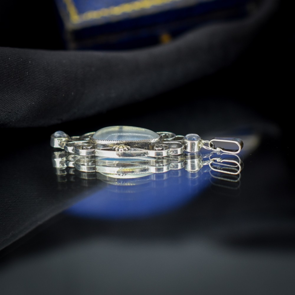 An antique sterling silver drop pendant featuring openwork scroll design set with an oval central moonstone cabochon and two smaller round moonstones. View VI