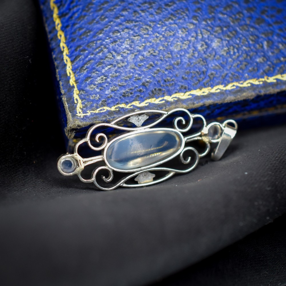 An antique sterling silver drop pendant featuring openwork scroll design set with an oval central moonstone cabochon and two smaller round moonstones. View VII