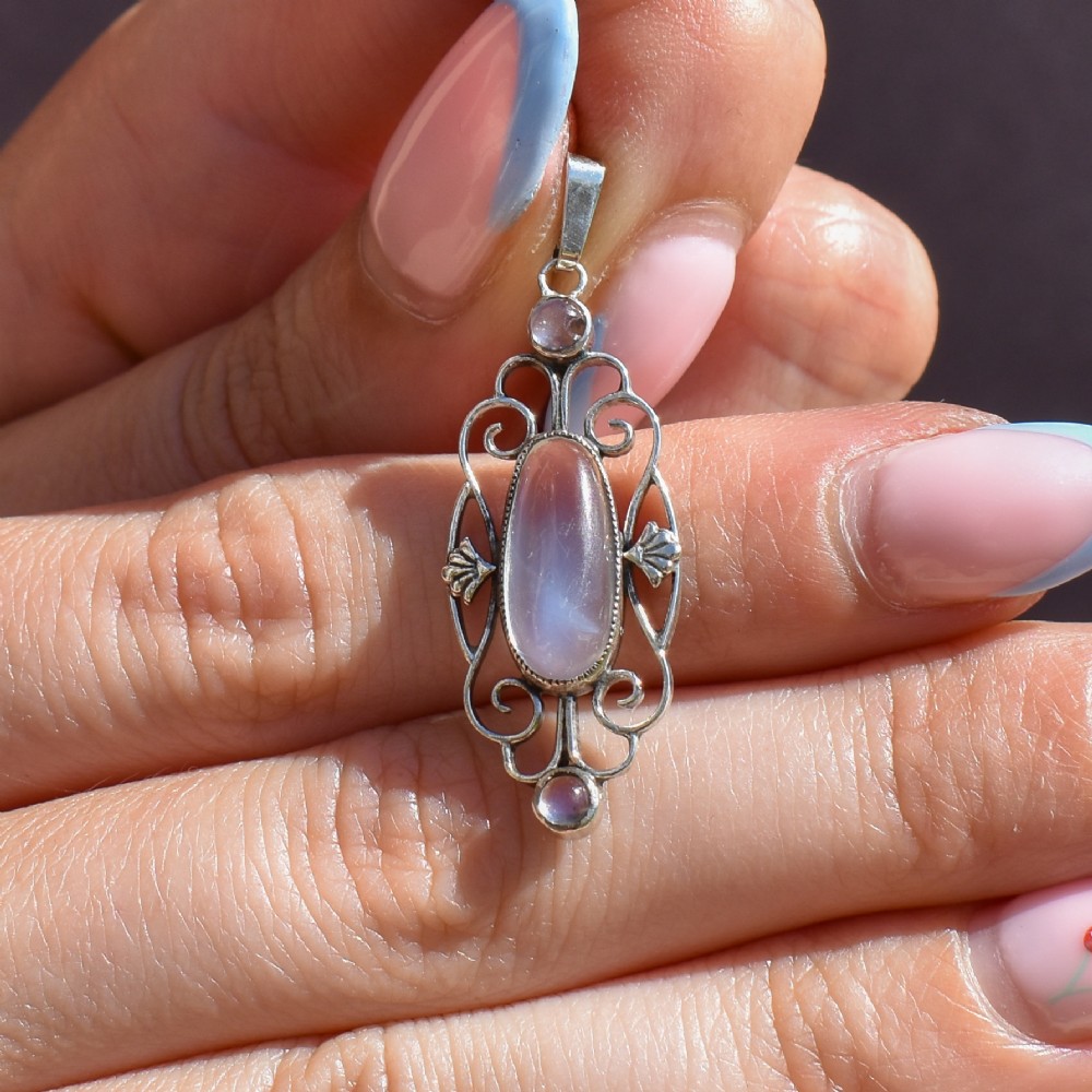 An antique sterling silver drop pendant featuring openwork scroll design set with an oval central moonstone cabochon and two smaller round moonstones. View VIII