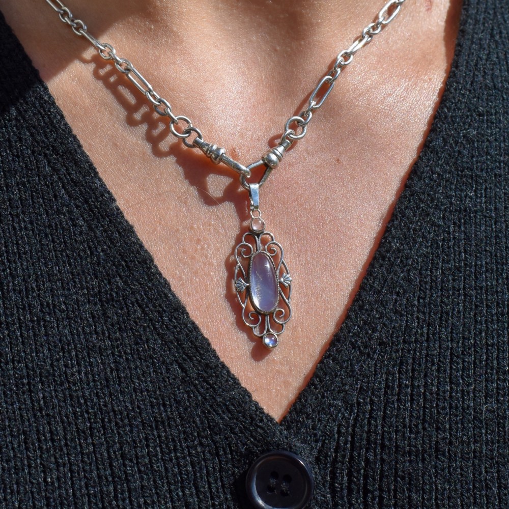An antique sterling silver drop pendant featuring openwork scroll design set with an oval central moonstone cabochon and two smaller round moonstones. View IX