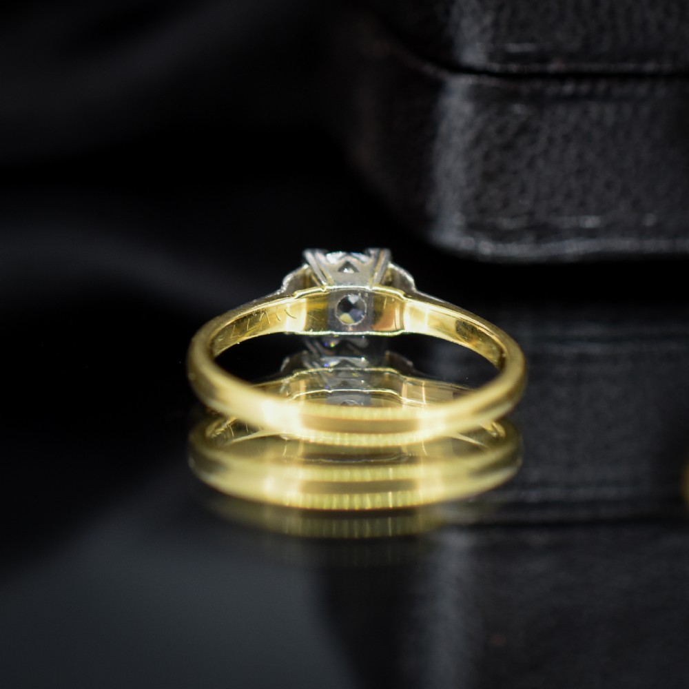 An Art Deco engagement ring featuring a square-set central old cut diamond on an 18ct yellow gold band with white metal stepped shoulders. View V