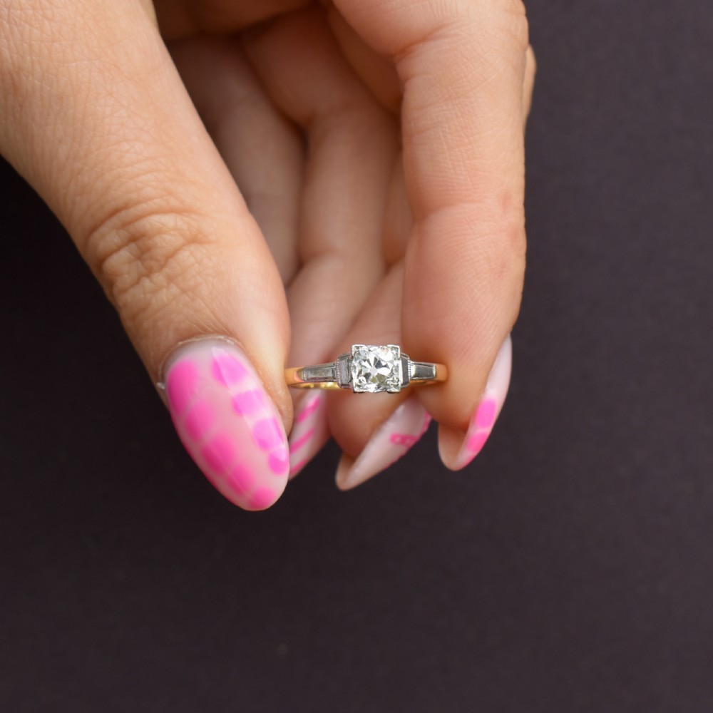 An Art Deco engagement ring featuring a square-set central old cut diamond on an 18ct yellow gold band with white metal stepped shoulders. View VI
