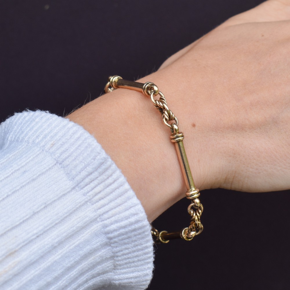 An antique 9ct yellow gold bracelet featuring elongated tubular bar links interspersed with love knot connections and a dog clip clasp. View IX