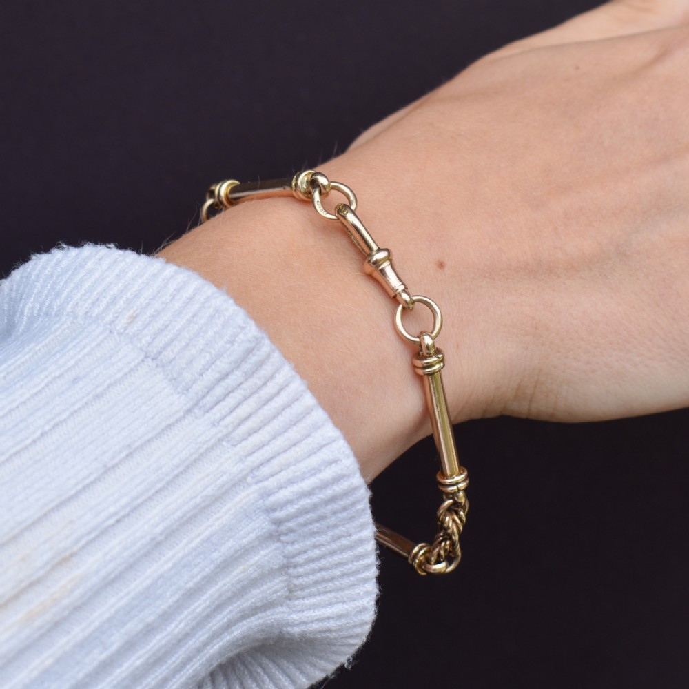 An antique 9ct yellow gold bracelet featuring elongated tubular bar links interspersed with love knot connections and a dog clip clasp. View X