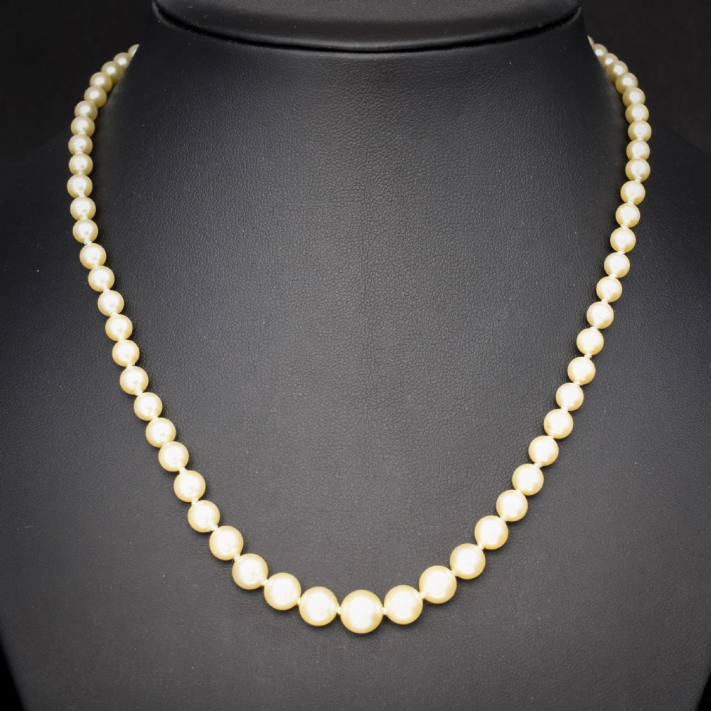 A 17-inch strand of graduated cream pearls featuring individually knotted beads and a gold bow-shaped clasp, resting on green velvet. View II