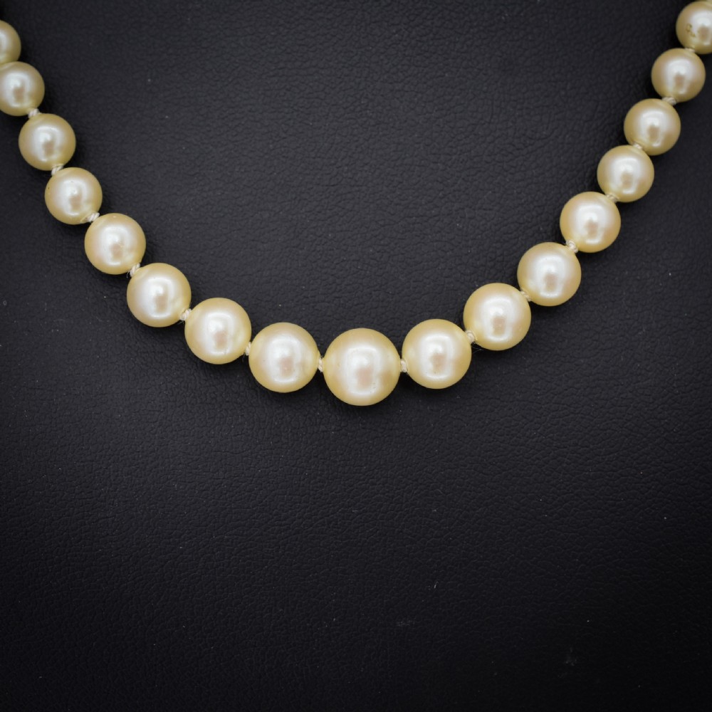 A 17-inch strand of graduated cream pearls featuring individually knotted beads and a gold bow-shaped clasp, resting on green velvet. View III