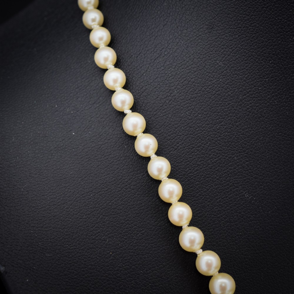A 17-inch strand of graduated cream pearls featuring individually knotted beads and a gold bow-shaped clasp, resting on green velvet. View IV