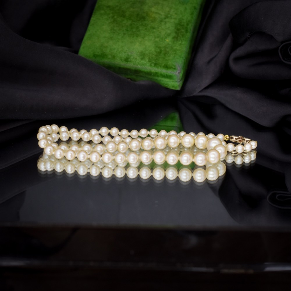 A 17-inch strand of graduated cream pearls featuring individually knotted beads and a gold bow-shaped clasp, resting on green velvet. View VI