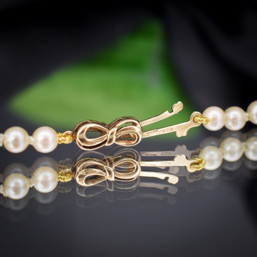 A 17-inch strand of graduated cream pearls featuring individually knotted beads and a gold bow-shaped clasp, resting on green velvet. View VII