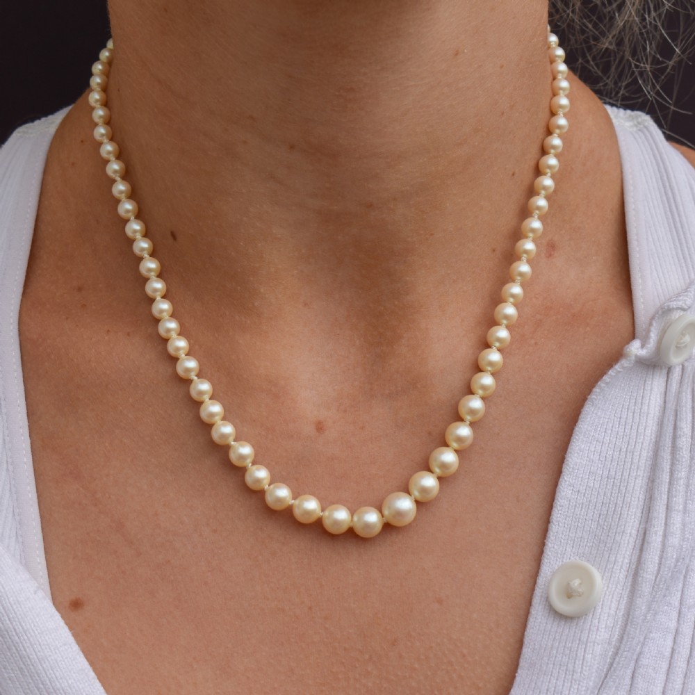 A 17-inch strand of graduated cream pearls featuring individually knotted beads and a gold bow-shaped clasp, resting on green velvet. View VIII