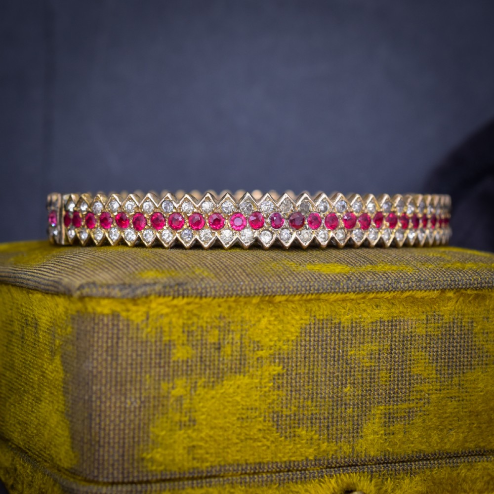 An Art Deco hinged bangle featuring a geometric chevron pattern set with alternating rows of clear and red round-cut paste stones.