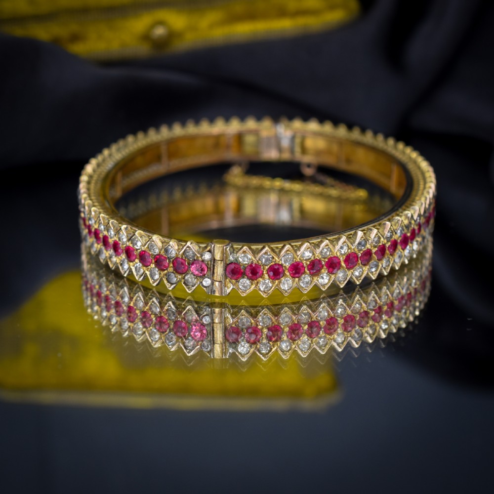 An Art Deco hinged bangle featuring a geometric chevron pattern set with alternating rows of clear and red round-cut paste stones. View IV