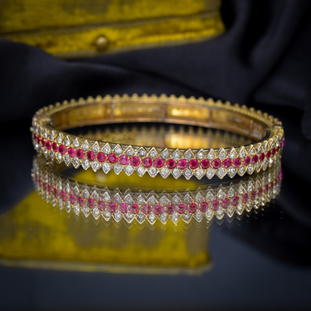 An Art Deco hinged bangle featuring a geometric chevron pattern set with alternating rows of clear and red round-cut paste stones. View V