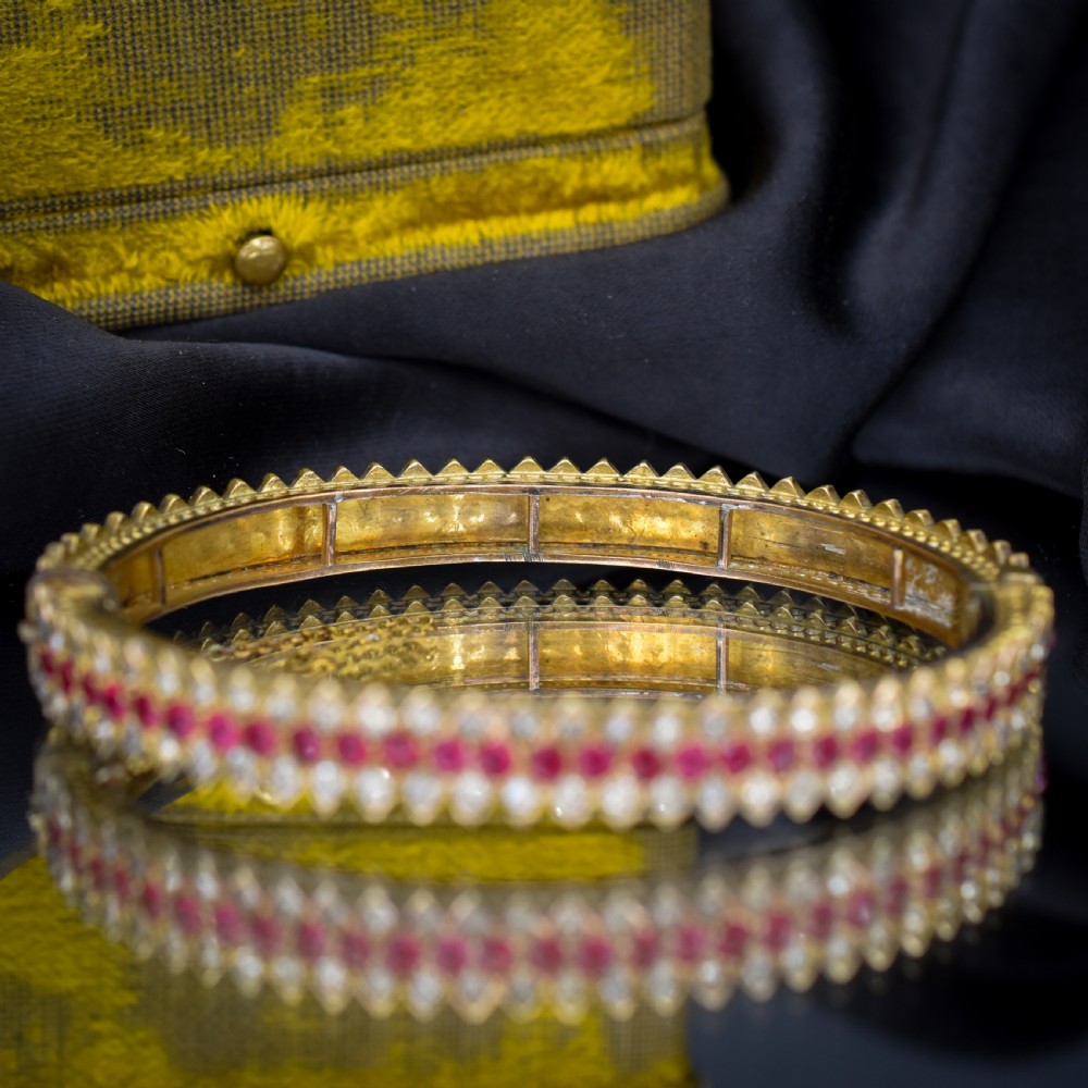 An Art Deco hinged bangle featuring a geometric chevron pattern set with alternating rows of clear and red round-cut paste stones. View VI