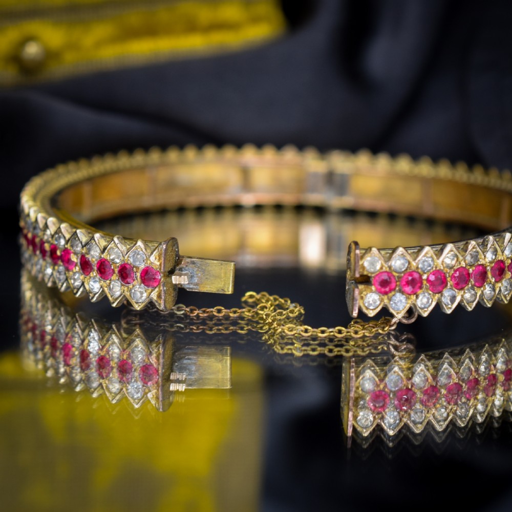An Art Deco hinged bangle featuring a geometric chevron pattern set with alternating rows of clear and red round-cut paste stones. View VII