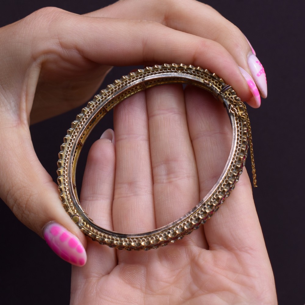 An Art Deco hinged bangle featuring a geometric chevron pattern set with alternating rows of clear and red round-cut paste stones. View VIII