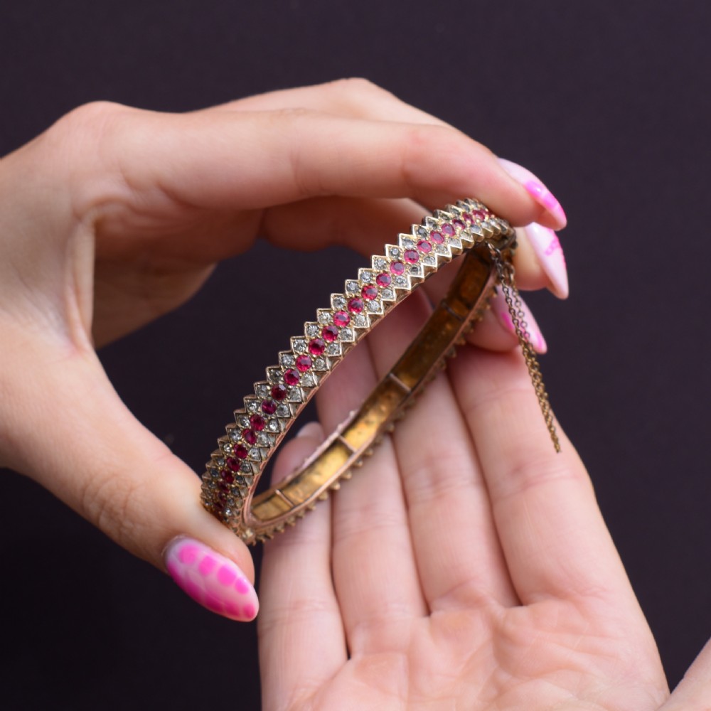 An Art Deco hinged bangle featuring a geometric chevron pattern set with alternating rows of clear and red round-cut paste stones. View IX