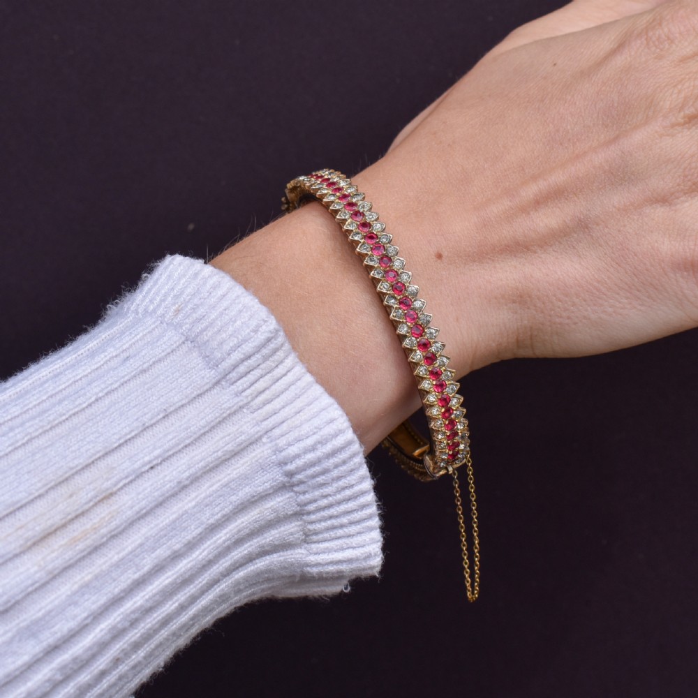 An Art Deco hinged bangle featuring a geometric chevron pattern set with alternating rows of clear and red round-cut paste stones. View XI