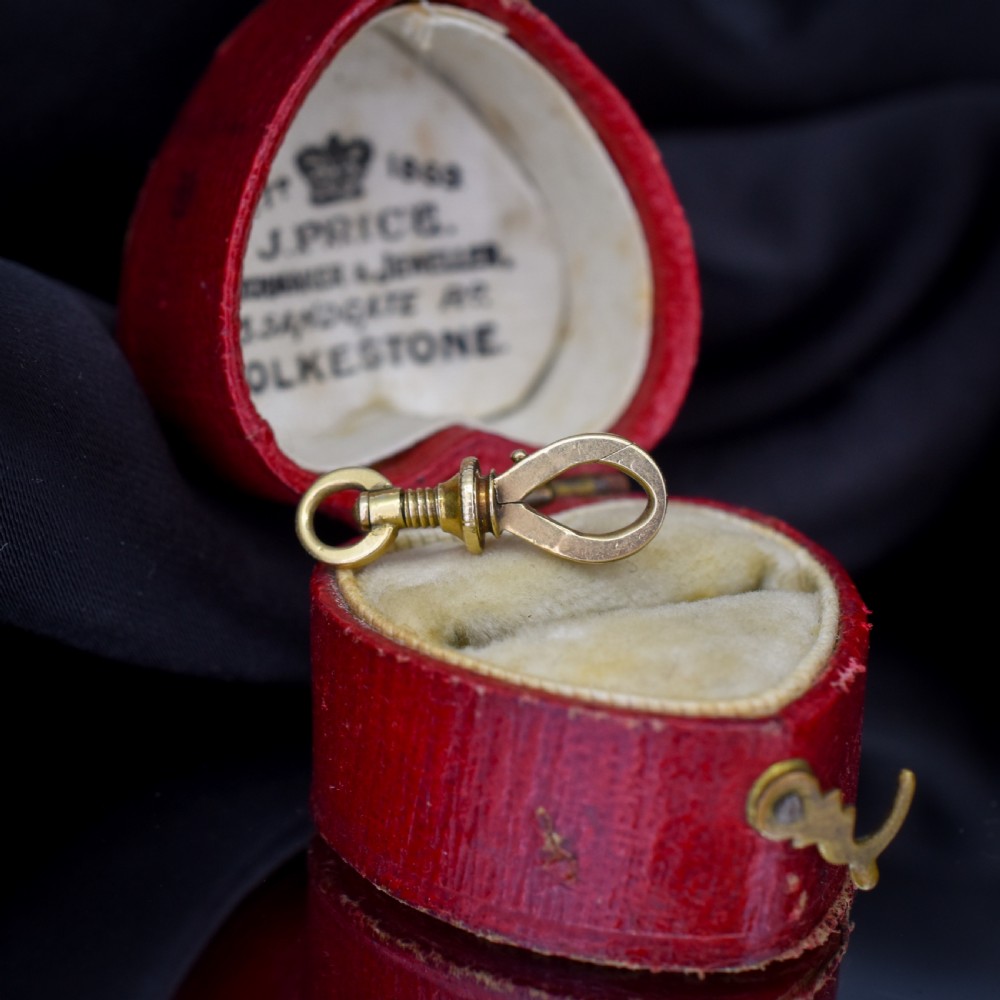 An antique 15ct yellow gold screw dog clip fastener resting on a red heart-shaped presentation box.