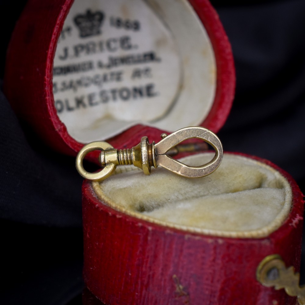 An antique 15ct yellow gold screw dog clip fastener resting on a red heart-shaped presentation box. View II