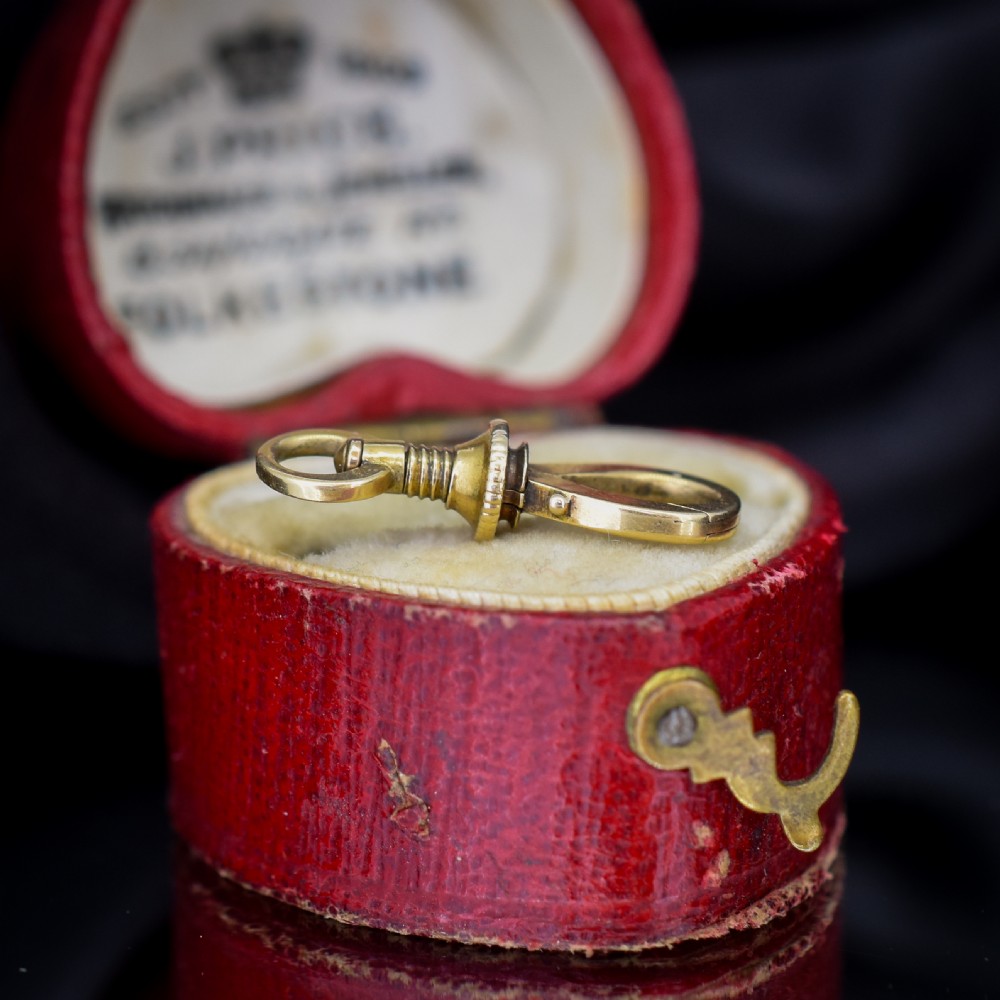 An antique 15ct yellow gold screw dog clip fastener resting on a red heart-shaped presentation box. View III